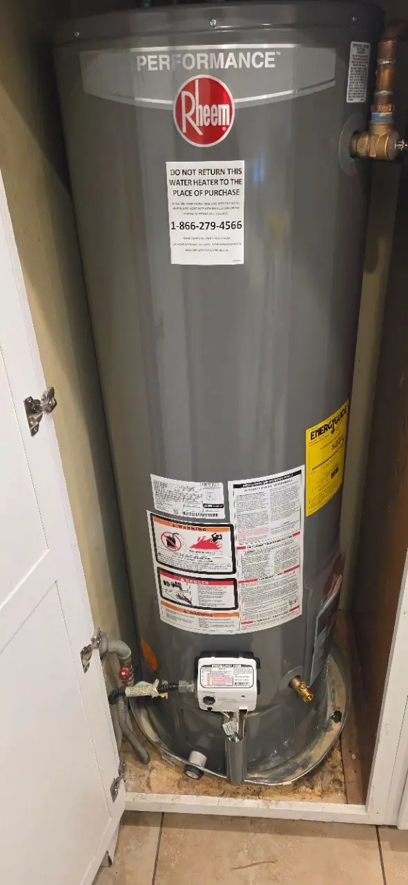 Newly installed Rheem gas water heater in a cabinet closet with copper and flexible supply lines connected.