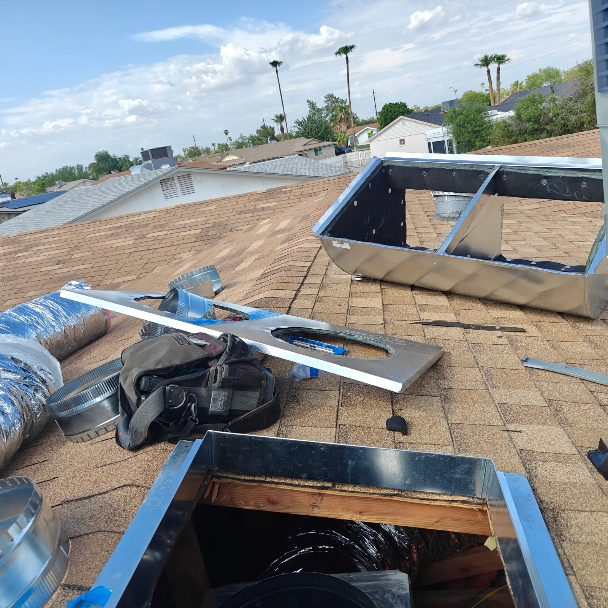 Rooftop ductwork installation in progress with sheet metal boots and flex duct laid out on shingles.