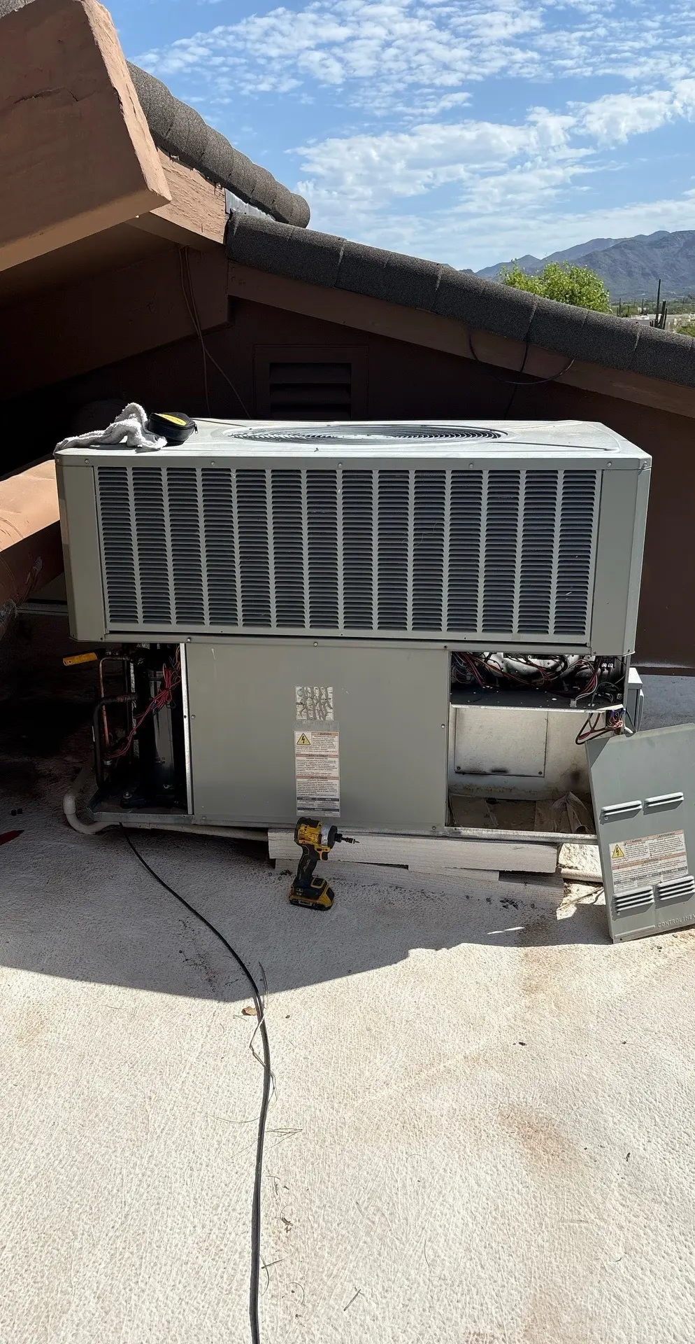 Rooftop packaged HVAC unit with access panels removed during service, with mountains in the background.