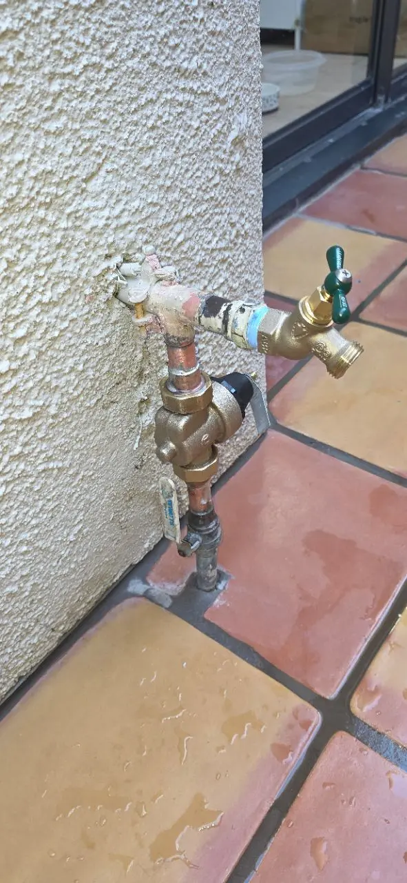 A newly installed exterior brass hose bib and pressure regulator on a stucco wall by a sliding glass door.