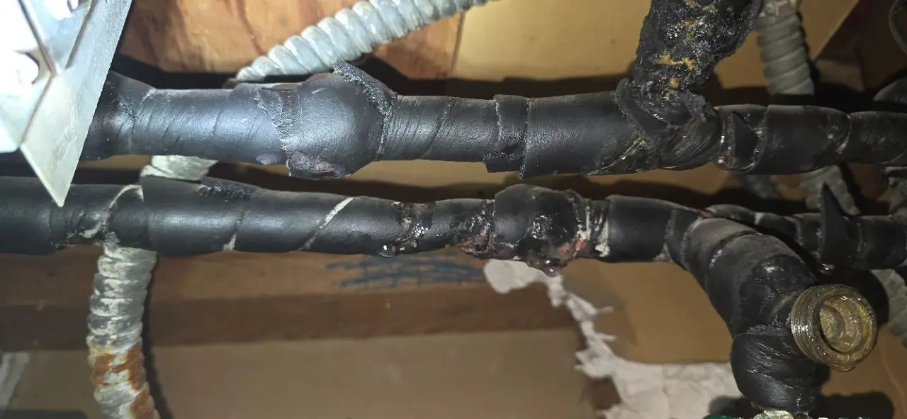 Aged insulated piping showing corrosion and staining running through a framed opening near flexible conduit.